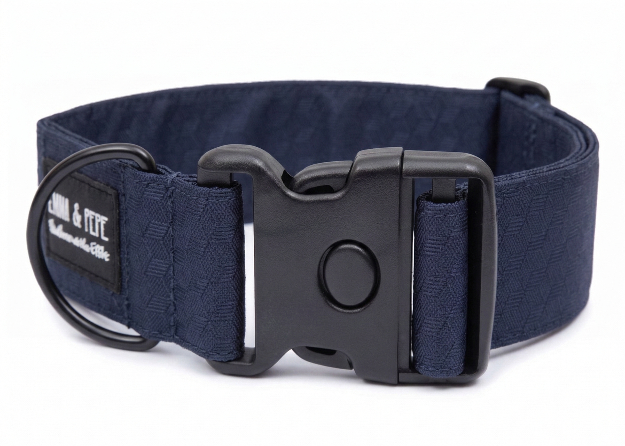 Dunkelblaues Hundehalsband aus Stoff mit schwarzem Kunststoff-Schnellverschluss und schwarzem Metallring zur Befestigung einer Leine. Das Halsband ist vor weißem Hintergrund fotografiert und zeigt eine breite, verstellbare Ausführung mit gepolsterter Innenseite. Auf einem kleinen Etikett am Ring ist ein Markenlogo zu erkennen.