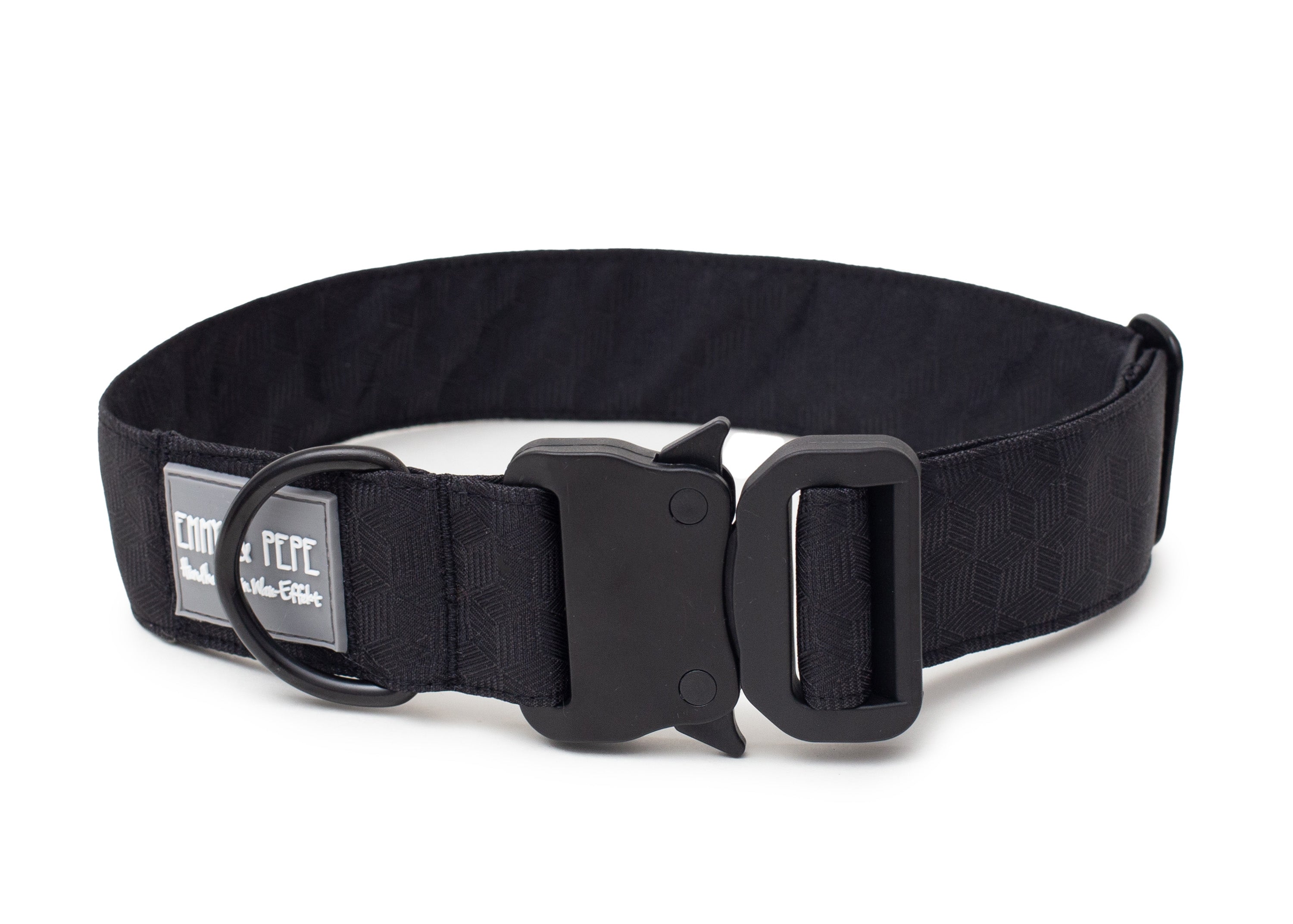 Schwarzes Hundehalsband aus Stoff mit schwarzem Kunststoff-Sicherheitsverschluss und schwarzem Metallring zur Befestigung einer Leine. Das Halsband ist vor weißem Hintergrund fotografiert und zeigt eine breite, verstellbare Ausführung mit gepolsterter Innenseite. Auf einem kleinen Etikett am Ring ist ein Markenlogo zu erkennen.