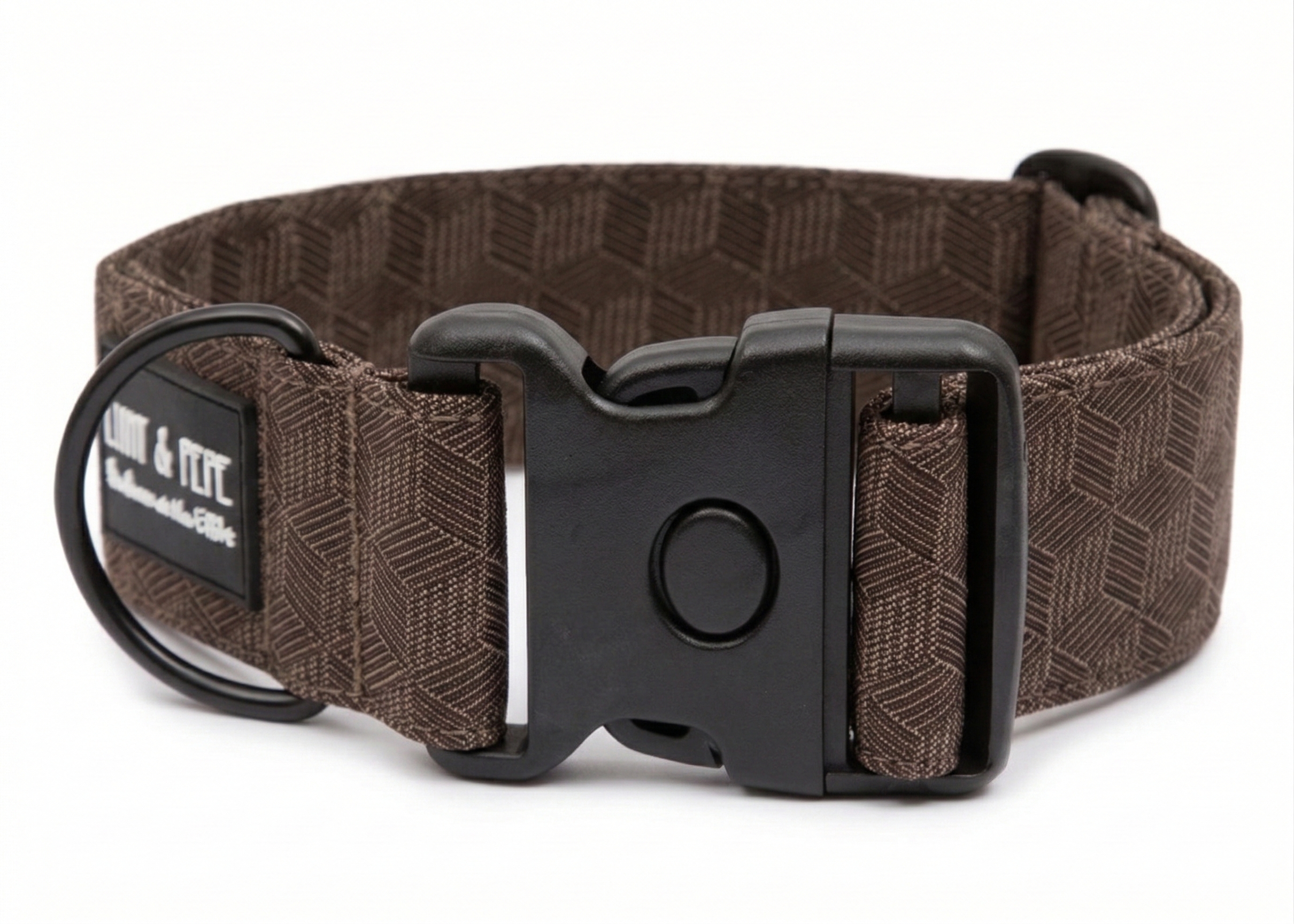 Braunes Hundehalsband aus Stoff mit schwarzem Kunststoff-Schnellverschluss und schwarzem Metallring zur Befestigung einer Leine. Das Halsband ist vor weißem Hintergrund fotografiert und zeigt eine breite, verstellbare Ausführung mit gepolsterter Innenseite. Auf einem kleinen Etikett am Ring ist ein Markenlogo zu erkennen.