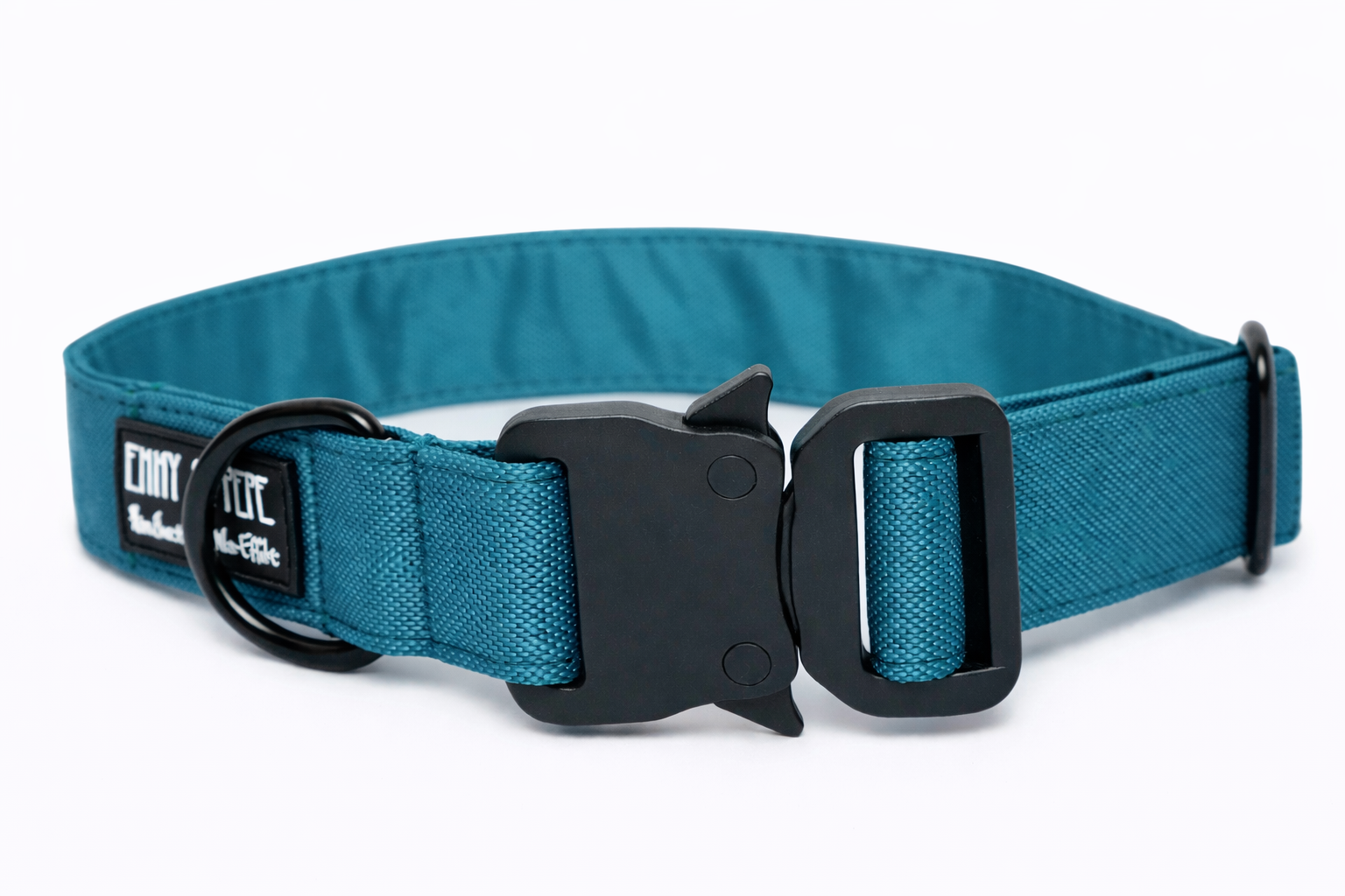 Blaues Hundehalsband aus Stoff mit schwarzem Kunststoff-Sicherheitsverschluss und schwarzem Metallring zur Befestigung einer Leine. Das Halsband ist vor weißem Hintergrund fotografiert und zeigt eine breite, verstellbare Ausführung mit gepolsterter Innenseite. Auf einem kleinen Etikett am Ring ist ein Markenlogo zu erkennen.