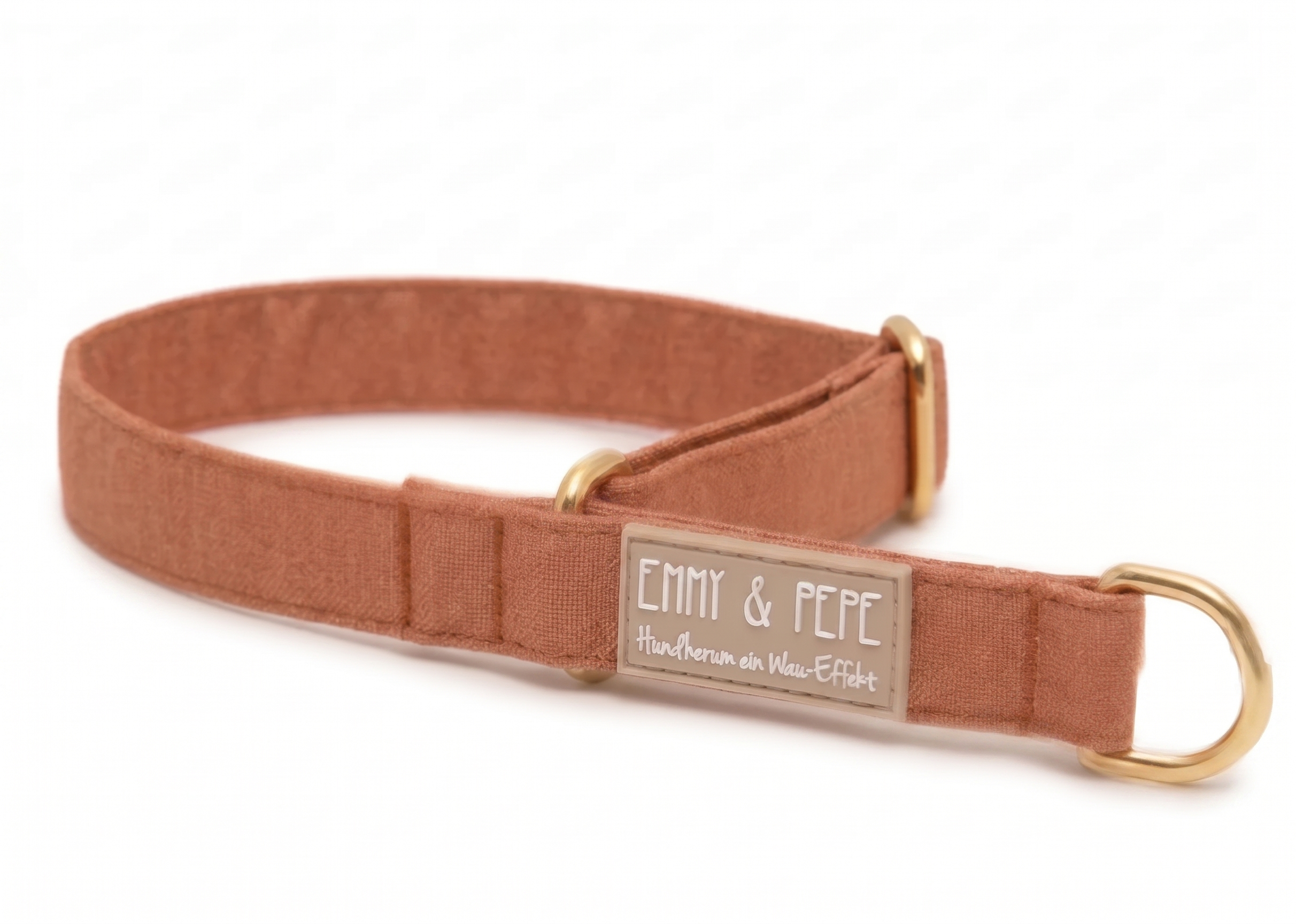 Ein rostbraunes Hundehalsband aus Stoff mit goldenen Beschlägen liegt auf weißem Grund. Auf einem beige-grauen Gummipatch steht das Logo „EMMY & PEPE“ und darunter der Slogan „Hundherum ein Wau-Effekt“.