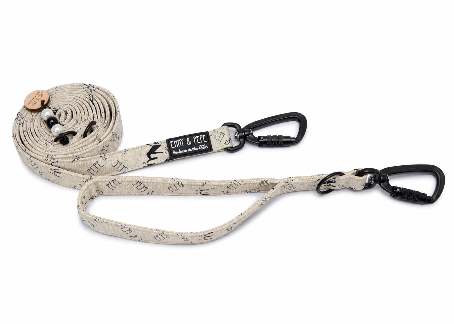Creme Hundeleine von Emmy & Pepe mit dezentem Allover-Muster und schwarzer Hardware auf hellem Hintergrund. Die Leine ist zusammengerollt dargestellt und verfügt über zwei Sicherheitskarabiner, einem integrierten Kurzführer sowie dekorative Perlen und einen Holzanhänger am oberen Ende.