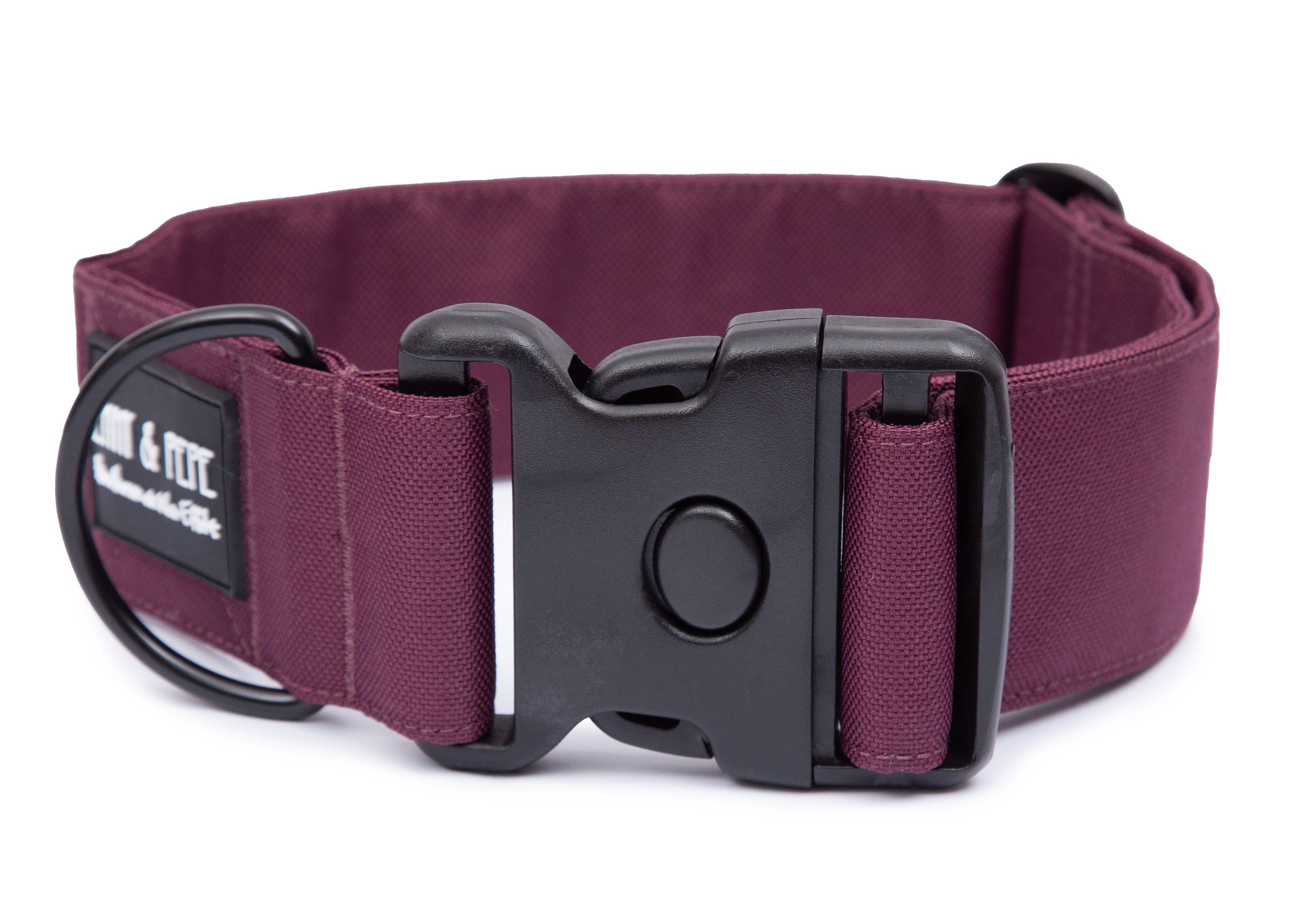 Weinrotes Hundehalsband aus Stoff mit schwarzem Kunststoff-Schnellverschluss und schwarzem Metallring zur Befestigung einer Leine. Das Halsband ist vor weißem Hintergrund fotografiert und zeigt eine breite, verstellbare Ausführung mit gepolsterter Innenseite. Auf einem kleinen Etikett am Ring ist ein Markenlogo zu erkennen.