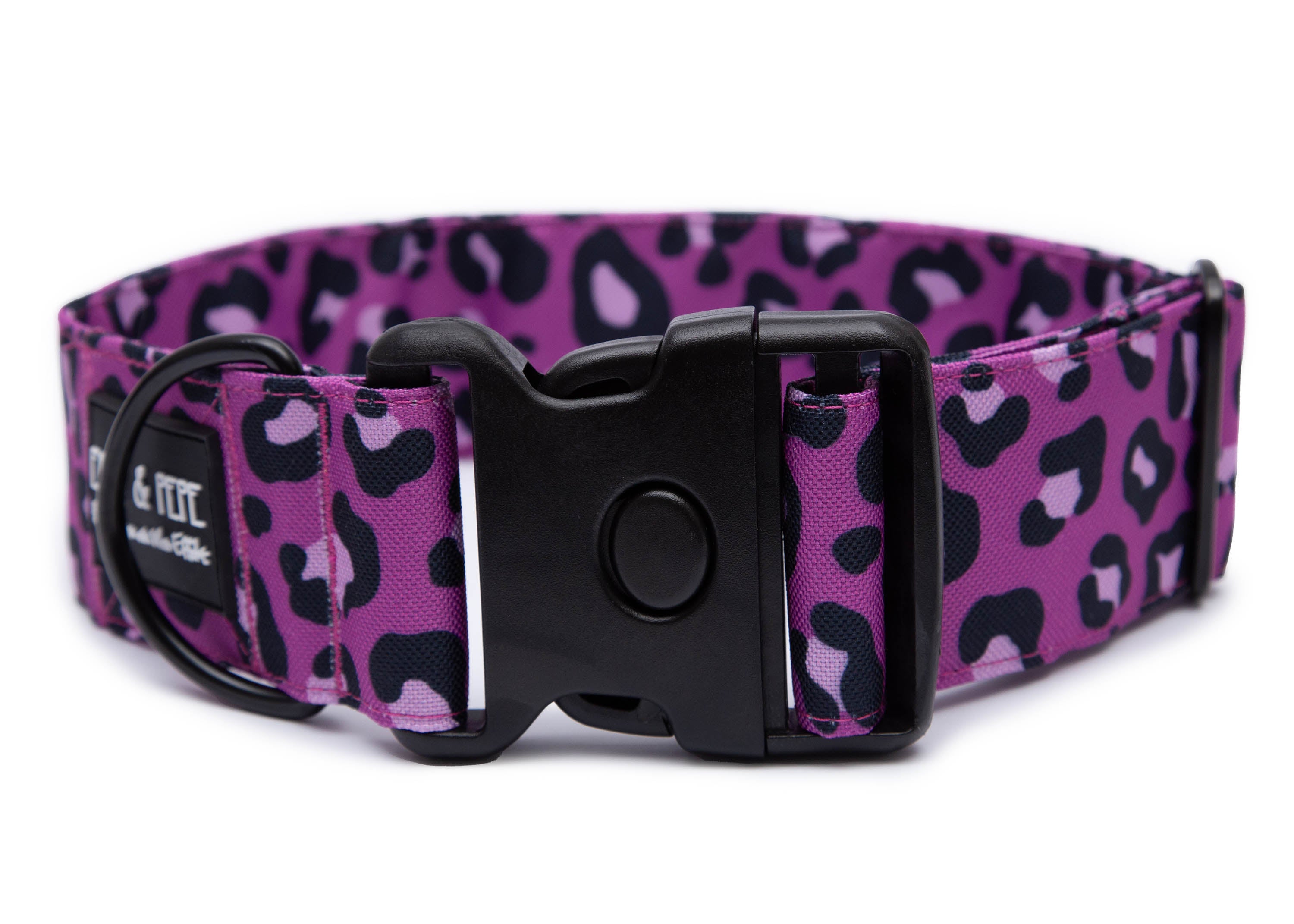 Fuchsiafarbenes Hundehalsband mit Leomuster aus Stoff mit schwarzem Kunststoff-Schnellverschluss und schwarzem Metallring zur Befestigung einer Leine. Das Halsband ist vor weißem Hintergrund fotografiert und zeigt eine breite, verstellbare Ausführung mit gepolsterter Innenseite. Auf einem kleinen Etikett am Ring ist ein Markenlogo zu erkennen.