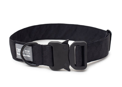 Schwarzes Hundehalsband aus Stoff mit schwarzem Kunststoff-Sicherheitsverschluss und schwarzem Metallring zur Befestigung einer Leine. Das Halsband ist vor weißem Hintergrund fotografiert und zeigt eine breite, verstellbare Ausführung mit gepolsterter Innenseite. Auf einem kleinen Etikett am Ring ist ein Markenlogo zu erkennen.