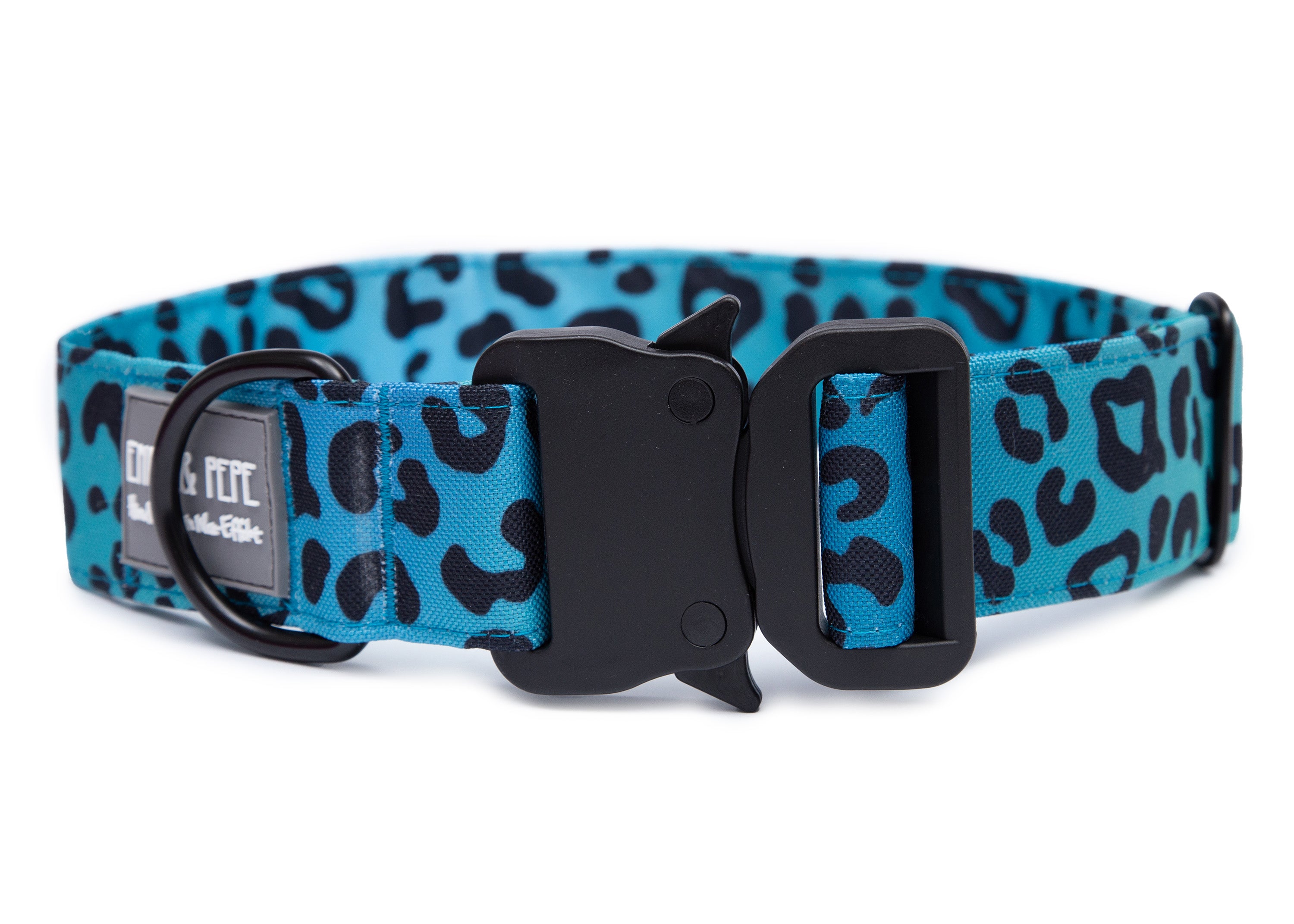 Blaues Hundehalsband in Leomuster aus Stoff mit schwarzem Kunststoff-Sicherheitsverschluss und schwarzem Metallring zur Befestigung einer Leine. Das Halsband ist vor weißem Hintergrund fotografiert und zeigt eine breite, verstellbare Ausführung mit gepolsterter Innenseite. Auf einem kleinen Etikett am Ring ist ein Markenlogo zu erkennen.