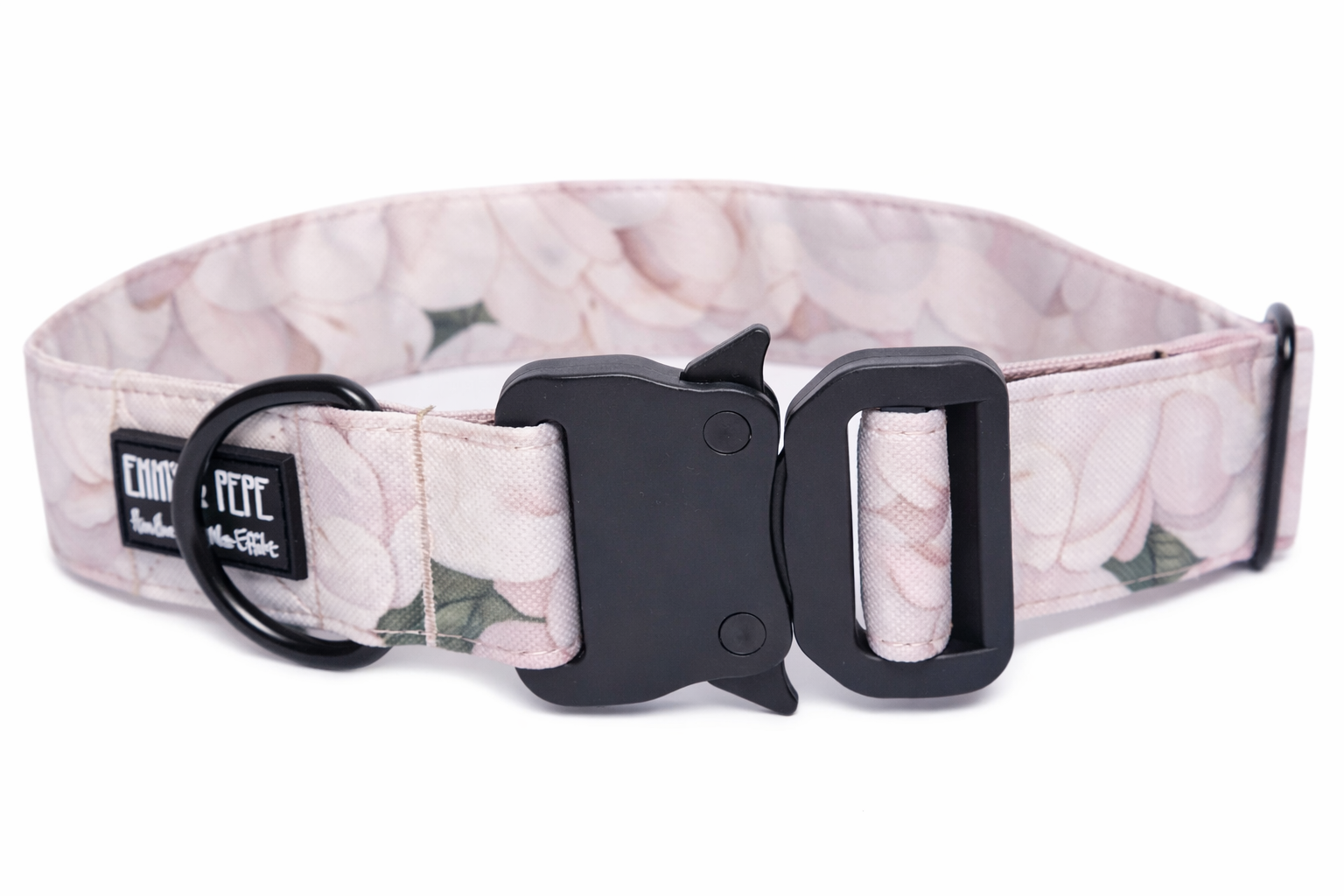 Florales Hundehalsband aus Stoff mit schwarzem Kunststoff-Sicherheitsverschluss und schwarzem Metallring zur Befestigung einer Leine. Das Halsband ist vor weißem Hintergrund fotografiert und zeigt eine breite, verstellbare Ausführung mit gepolsterter Innenseite. Auf einem kleinen Etikett am Ring ist ein Markenlogo zu erkennen.
