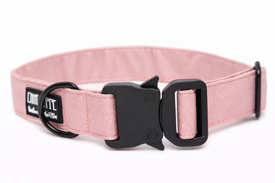 Rosanes Hundehalsband aus Stoff mit schwarzem Kunststoff-Sicherheitsverschluss und schwarzem Metallring zur Befestigung einer Leine. Das Halsband ist vor weißem Hintergrund fotografiert und zeigt eine breite, verstellbare Ausführung mit gepolsterter Innenseite. Auf einem kleinen Etikett am Ring ist ein Markenlogo zu erkennen.