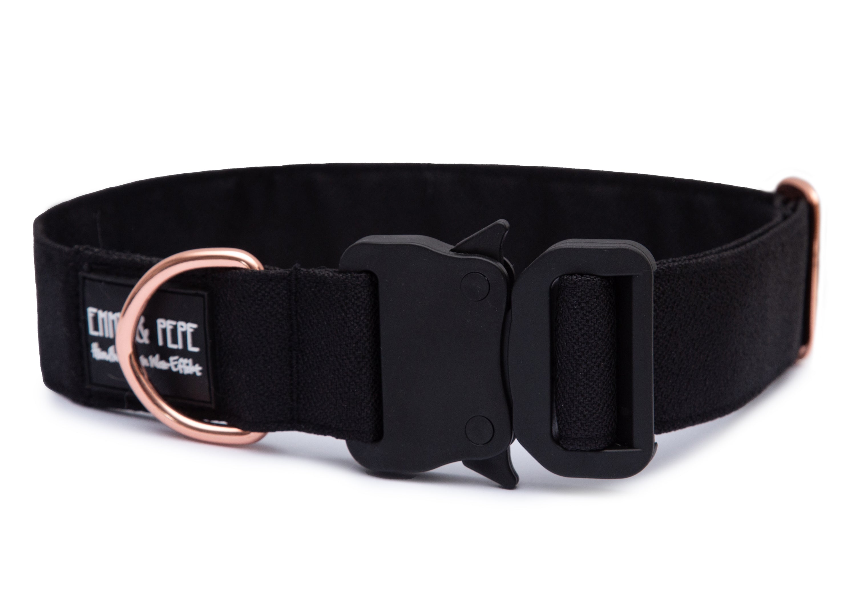 Schwarzes Hundehalsband aus Stoff mit schwarzem Kunststoff-Sicherheitsverschluss und rosegoldenem Metallring zur Befestigung einer Leine. Das Halsband ist vor weißem Hintergrund fotografiert und zeigt eine breite, verstellbare Ausführung mit gepolsterter Innenseite. Auf einem kleinen Etikett am Ring ist ein Markenlogo zu erkennen.