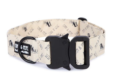 Cremefarbenes Hundehalsband mit Wau-Effekt Aufdruck aus Stoff mit schwarzem Kunststoff-Sicherheitsverschluss und schwarzem Metallring zur Befestigung einer Leine. Das Halsband ist vor weißem Hintergrund fotografiert und zeigt eine breite, verstellbare Ausführung mit gepolsterter Innenseite. Auf einem kleinen Etikett am Ring ist ein Markenlogo zu erkennen.