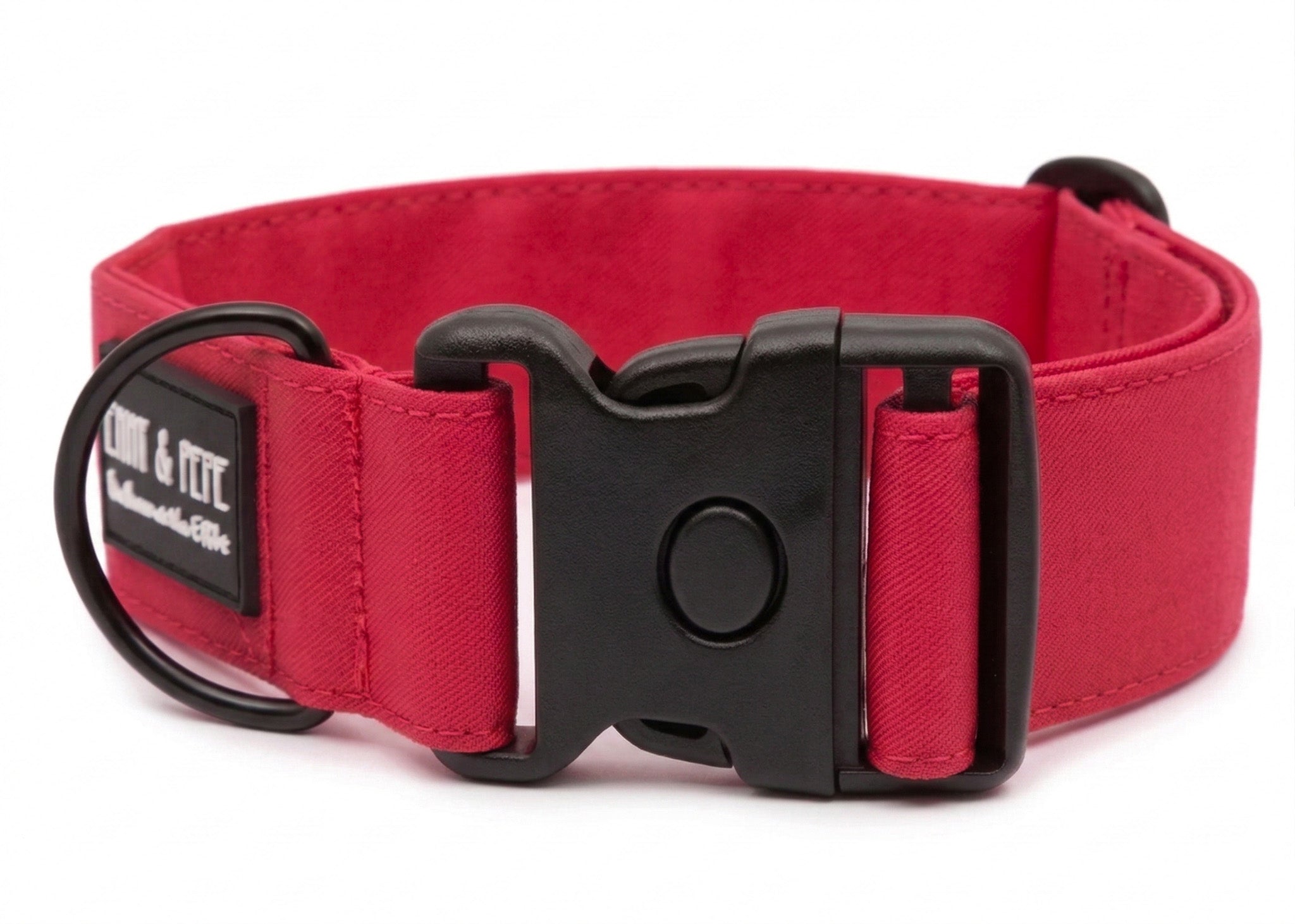 Neon Pinkes Hundehalsband aus Stoff mit schwarzem Kunststoff-Schnellverschluss und schwarzem Metallring zur Befestigung einer Leine. Das Halsband ist vor weißem Hintergrund fotografiert und zeigt eine breite, verstellbare Ausführung mit gepolsterter Innenseite. Auf einem kleinen Etikett am Ring ist ein Markenlogo zu erkennen.