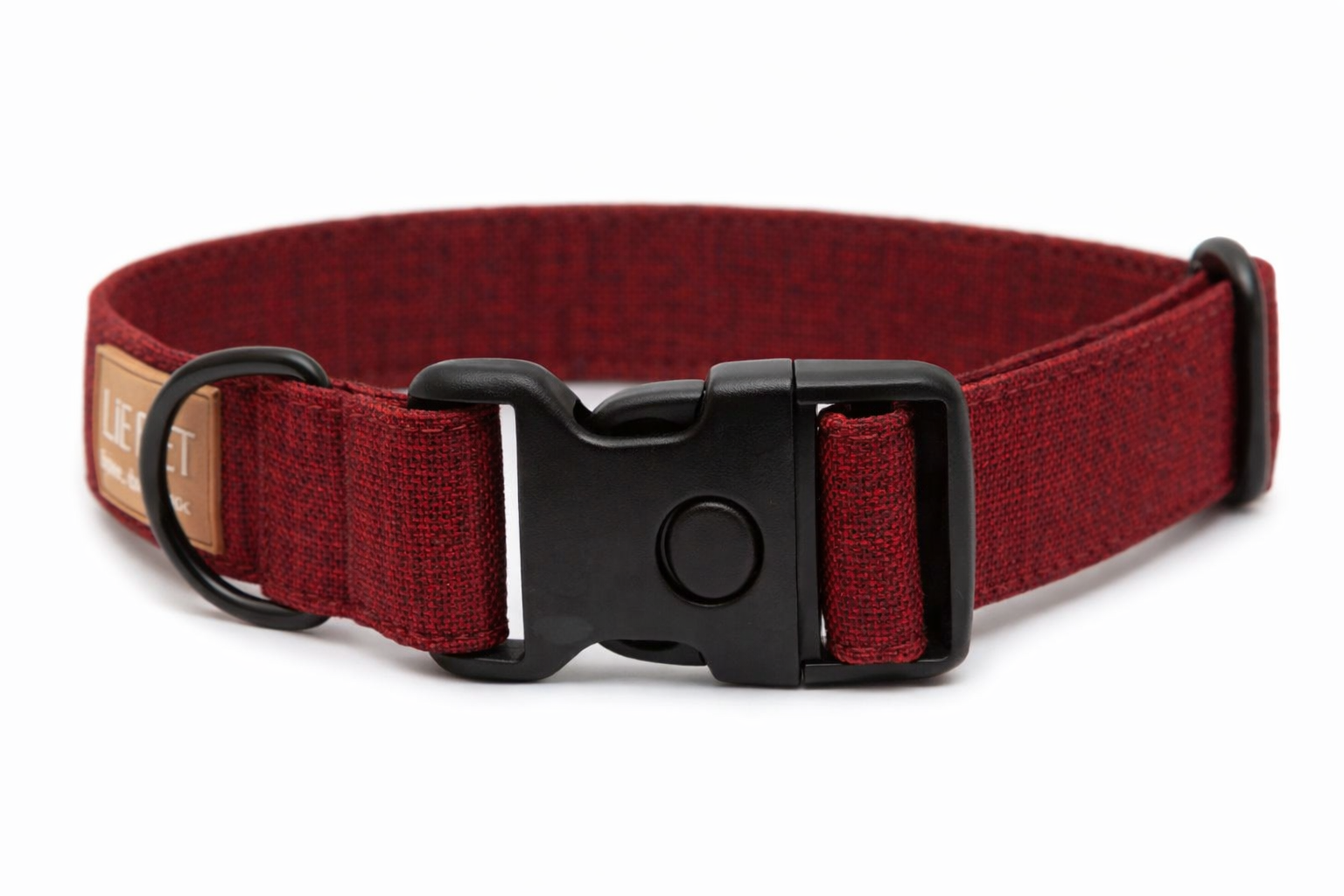 Bordeauxfarbenes Hundehalsband aus Stoff mit schwarzem Kunststoff-Schnellverschluss und schwarzem Metallring zur Befestigung einer Leine. Das Halsband ist vor weißem Hintergrund fotografiert und zeigt eine breite, verstellbare Ausführung mit gepolsterter Innenseite. Auf einem kleinen Etikett am Ring ist ein Markenlogo zu erkennen.