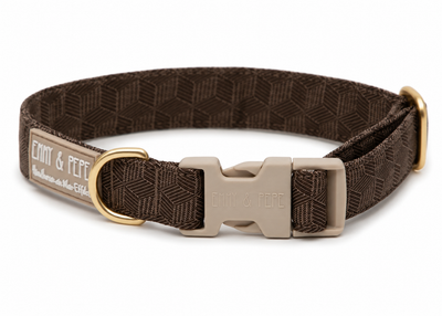 Braunes Hundehalsband von Emmy & Pepe mit geometrischem Muster und beigefarbener Kunststoffschnalle auf weißem Hintergrund. Das Halsband verfügt über goldfarbene Metallringe sowie ein beiges Markenlabel mit weißem Schriftzug.