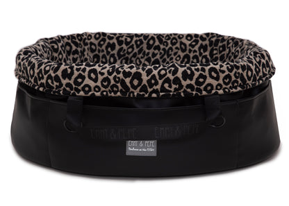  Wau-Snuggle Reisebett mit robustem schwarzen Kunstleder an der Außenseite und einem weichen, beigen Innenfutter mit schwarzem Leopardenmuster in oval - Rand umgeklappt