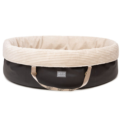 Freigestelltes ovales Wau-Snuggle Cord Creme Hundekörbchen für unterwegs von EMMY & PEPE mit dunklem Kunstleder und weichem cremefarbenem Cordstoff innen.