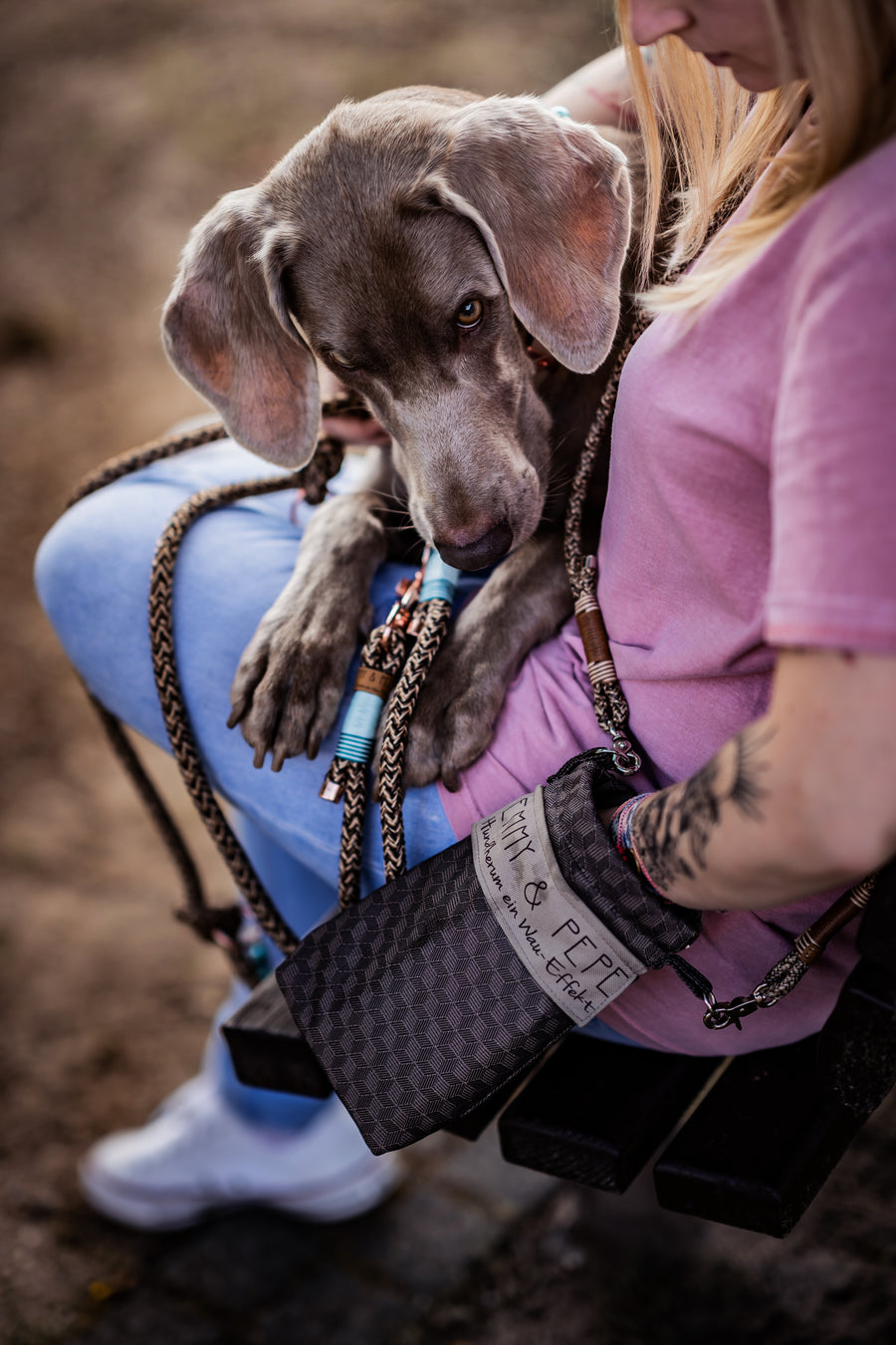 Weimaraner-Welpe kuschelt sich an sein Frauchen, die dunkle Wau-to-go von EMMY & PEPE mit geometrischem Muster hängt am geflochtenen Gurt